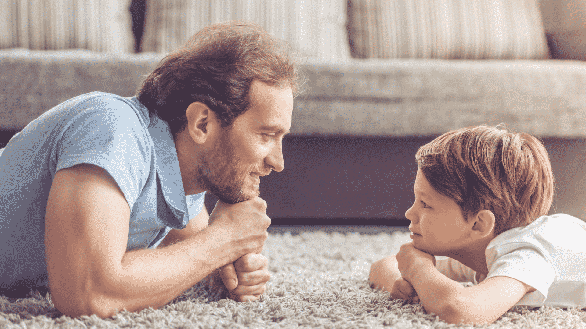 Adult male and little boy lying on carpet staring at each other